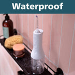 Waterproof cordless water flosser on a bathroom shelf with pink tiles.