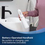 Person holding a white handheld battery-operated water flosser over a bathroom sink.