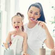 Smiling mother and daughter brushing their teeth together for healthy oral hygiene.