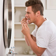 A man using dental floss in front of a bathroom mirror for oral hygiene.