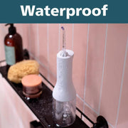 Waterproof cordless water flosser on a bathroom shelf with pink tiles.