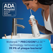 Woman using a cordless water flosser for oral hygiene near a bathroom sink.