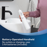 Person holding a white handheld battery-operated water flosser over a bathroom sink.