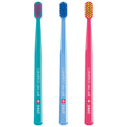 Three colorful Curaprox ultra soft toothbrushes in teal, light blue, and pink.